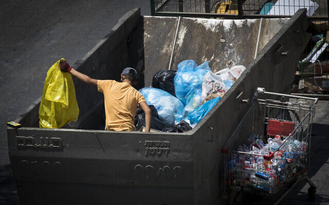 A teenager search for cans through a garbage container in the center of Jerusalem on July 13,2020 (Olivier Fitoussi/Flash90) A teenager search for cans through a garbage container in the center of Jerusalem on July 13,2020 (Olivier Fitoussi/Flash90)