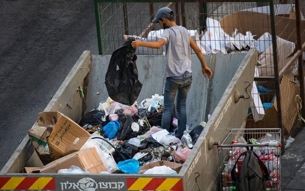 A teenager search for cans through a garbage container in the center of Jerusalem on September 02,2020. (Nati Shohat/Flash90) A teenager search for cans through a garbage container in the center of Jerusalem on September 02,2020. (Nati Shohat/Flash90)