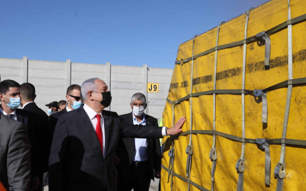 Prime Minister Benjamin Netanyahu touches the first batch of Pfizer vaccines to arrive in Israel at Ben Gurion Airport near Tel Aviv, December 9, 2020. (Marc Israel Sellem/Pool)