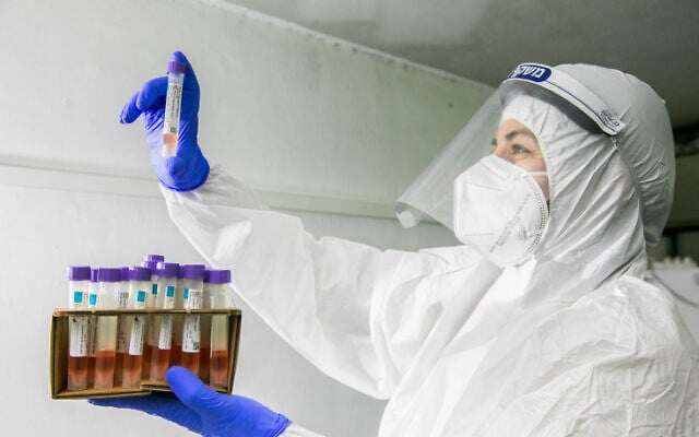 A Maccabi health care worker carries coronavirus test samples in Rehovot on December 15, 2020. (Yossi Aloni/Flash90) A Maccabi health care worker carries coronavirus test samples in Rehovot on December 15, 2020. (Yossi Aloni/Flash90)