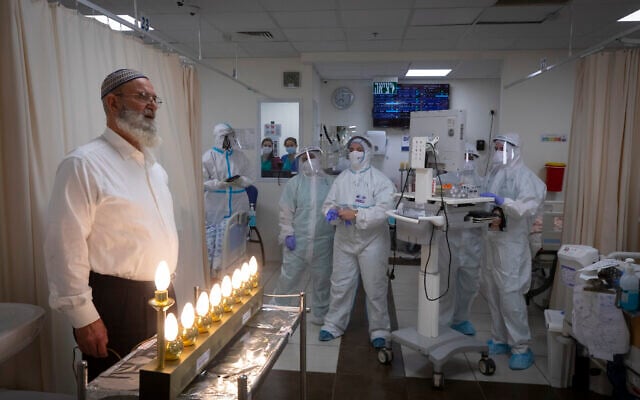 Staff at Shaare Zedek Medical Center and patients light Hanukkah candles at the hospital's coronavirus ward in Jerusalem on December 17, 2020 (Olivier Fitoussi/Flash90) Staff at Shaare Zedek Medical Center and patients light Hanukkah candles at the hospital's coronavirus ward in Jerusalem on December 17, 2020 (Olivier Fitoussi/Flash90)