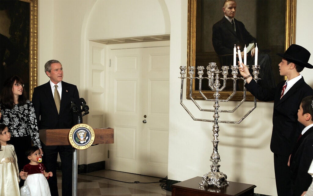 President George W. Bush looks on as 13-year-old Menachem Felzenberg, right, lights a menorah before the annual White House Hanukkah Reception on Thursday, Dec. 9, 2004 in Washington. (AP Photo/Evan Vucci)