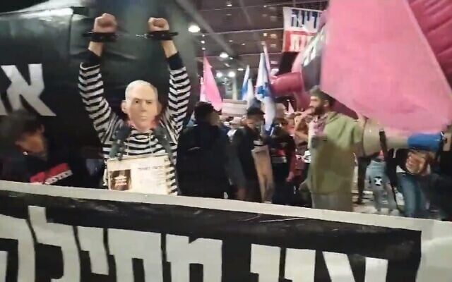 A man dressed as Prime Minister Benjamin Netanyahu in chains and a prison uniform standing in front of an inflatable submarine at a march between the Tel Aviv suburbs of Ramat Gan and Givatayim on Thursday, December 4, 2020. (Screengrab: Twitter) A man dressed as Prime Minister Benjamin Netanyahu in chains and a prison uniform standing in front of an inflatable submarine at a march between the Tel Aviv suburbs of Ramat Gan and Givatayim on Thursday, December 4, 2020. (Screengrab: Twitter)