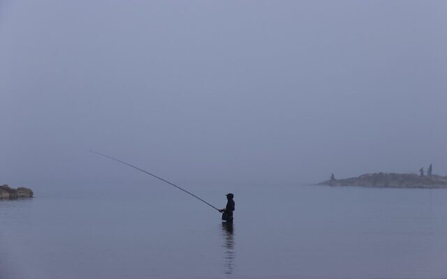 A man goes fishing amid morning fog in the coastal city of Netanya on January 6, 2021. (JACK GUEZ / AFP)