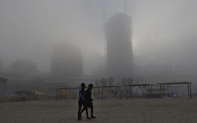 Two pedestrians walk on the beach early on January 6, 2021, in the coastal city of Netanya amid the morning fog on the first week of the new year. (JACK GUEZ / AFP)