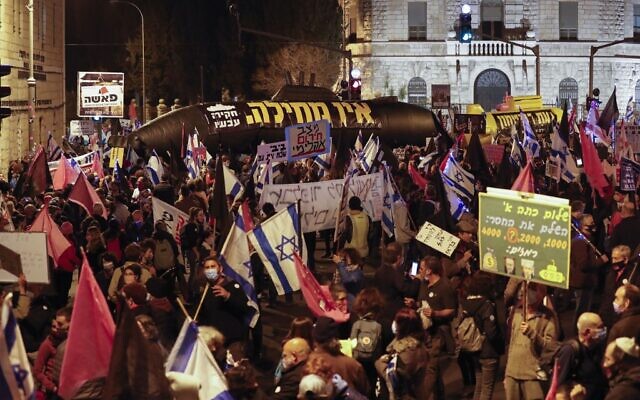 Israelis lift placards and flags as they protest against Prime Minister Benjamin Netanyahu outside his official residence in Jerusalem on January 9, 2021. (Ahmad Gharabli/AFP) Israelis lift placards and flags as they protest against Prime Minister Benjamin Netanyahu outside his official residence in Jerusalem on January 9, 2021. (Ahmad Gharabli/AFP)