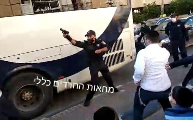 A police officer shoots in the air during a clash with ultra-Orthodox rioters protesting the enforcement of a lockdown ordered due to the coronavirus, in the city of Bnei Brak, January 24, 2021. (Screen capture: Twitter)