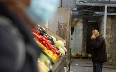 A man in a protective mask passes another man talking on his mobile phone at the Mahane Yehuda market in Jerusalem, December 23, 2020. (Maya Alleruzzo/AP)
