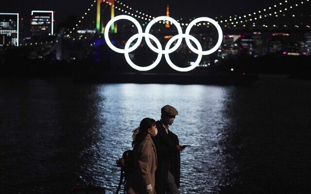 In this December 1, 2020 file photo, a man and a woman walk past near the Olympic rings floating in the water in the Odaiba section in Tokyo. (AP Photo/Eugene Hoshiko, File) In this December 1, 2020 file photo, a man and a woman walk past near the Olympic rings floating in the water in the Odaiba section in Tokyo. (AP Photo/Eugene Hoshiko, File)
