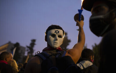 An anti-government protester wears a mask on the back of his head outside of the official residence of Prime Minister Benjamin Netanyahu on the day his corruption trial was originally scheduled before it was postponed, in Jerusalem, January 13, 2021. (Maya Alleruzzo/AP)