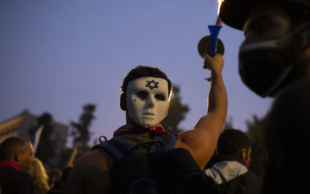 An anti-government protester wears a mask on the back of his head outside of the official residence of Prime Minister Benjamin Netanyahu on the day his corruption trial was originally scheduled before it was postponed, in Jerusalem, January 13, 2021. (Maya Alleruzzo/AP) An anti-government protester wears a mask on the back of his head outside of the official residence of Prime Minister Benjamin Netanyahu on the day his corruption trial was originally scheduled before it was postponed, in Jerusalem, January 13, 2021. (Maya Alleruzzo/AP)