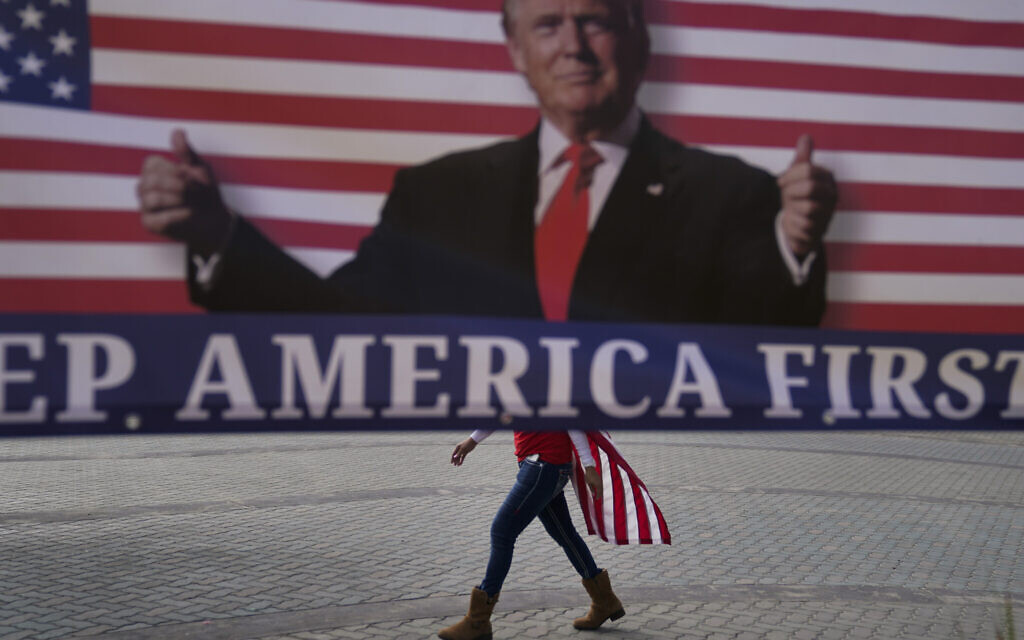 A woman draped in an American flag walks past a banner supporting US President Donald Trump during a rally on Jan. 6, 2021, in Huntington Beach, Calif. (AP/Jae C. Hong) A woman draped in an American flag walks past a banner supporting US President Donald Trump during a rally on Jan. 6, 2021, in Huntington Beach, Calif. (AP/Jae C. Hong)