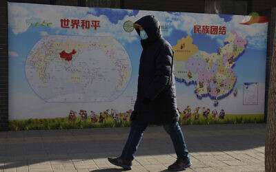 A man walks past a poster with the slogans 'World Peace' and 'Ethnic Unity' in Beijing, China, Jan. 11, 2021 (AP Photo/Ng Han Guan)