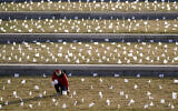 A man places flags at the National World War I Museum and Memorial Jan. 19, 2021, in Kansas City, Missouri. The 1,665 flags represent the area residents who died in the coronavirus pandemic and the display was part of a national memorial to lives lost to COVID-19. (AP Photo/Charlie Riedel)