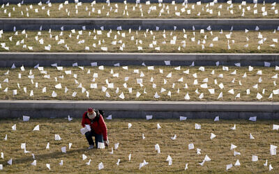 A man places flags at the National World War I Museum and Memorial Jan. 19, 2021, in Kansas City, Missouri. The 1,665 flags represent the area residents who died in the coronavirus pandemic and the display was part of a national memorial to lives lost to COVID-19. (AP Photo/Charlie Riedel)