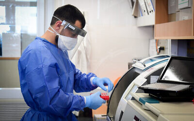 Illustrative -- Medical team worker at the Barzilay hospital in Ashkelon handles a coronavirus test sample on March 29, 2020 (Flash90)