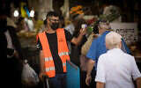 Illustrative: A man checks the temperature of a shopper at the entrance to the Mahane Yehuda Market in Jerusalem on June 18, 2020. (Yonatan Sindel/Flash90)
