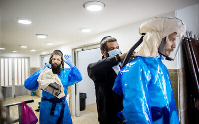 Workers from Chevra Kadisha Kehilat Yerushalayim, getting dressed with full protective gear to prepare a body before a funeral at a morgue for people who died from Covid-19, at the Sanhedriya Cemetery in Jerusalem, January 25, 2021. (Yonatan Sindel/Flash90)