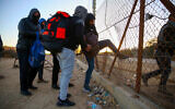 Palestinian workers from the West Bank city of Hebron carry personal belongings as they cross into Israel through a hole in  security fence near the West Bank city of Hebron, January 31, 2021. (Wisam Hashlamoun/Flash90)