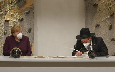 Rabbi Shaul Nekrich (R) and German Chancellor Angela Merkel (L) attend a ceremony to complete the historic Sulzbach Torah Scroll from 1792, rediscovered in 2015 and just restored, on the 76th anniversary of the liberation of Nazi Germany's Auschwitz death camp, on International Holocaust Remembrance Day, January 27, 2021 in Berlin, Germany. (Odd Andersen/Getty Images via JTA)