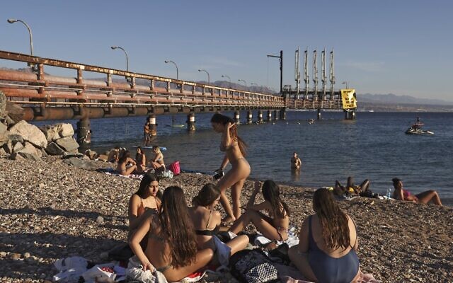 Youths sit together at a Red Sea beach by an abandoned oil jetty in Israel's southern port city of Eilat on February 10, 2021. (MENAHEM KAHANA / AFP)