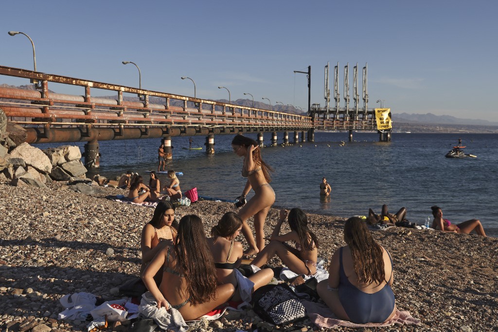 Youths sit together at a Red Sea beach by an abandoned oil jetty in Israel's southern port city of Eilat on February 10, 2021. (MENAHEM KAHANA / AFP) Youths sit together at a Red Sea beach by an abandoned oil jetty in Israel's southern port city of Eilat on February 10, 2021. (MENAHEM KAHANA / AFP)