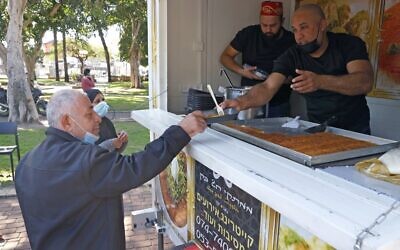 A man receives a slice of Knafe after getting vaccinated against the coronavirus in Tel Aviv-Jaffa, on February 16, 2021. (JACK GUEZ / AFP)