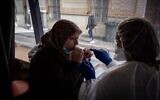 A patient (L) is watched by a medical assistant as she spits into a test tube for a COVID-19 saliva test on a roving bus in Saint-Etienne, France, on February 22, 2021. (Jean-Philippe Ksiazek/AFP)
