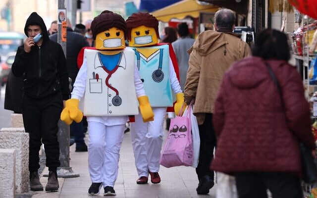 People dressed as Lego medical workers walk past shops in Jerusalem on February 24, 2021, a day before the Jewish holiday of Purim. (Emmanuel Dunand/AFP) People dressed as Lego medical workers walk past shops in Jerusalem on February 24, 2021, a day before the Jewish holiday of Purim. (Emmanuel Dunand/AFP)