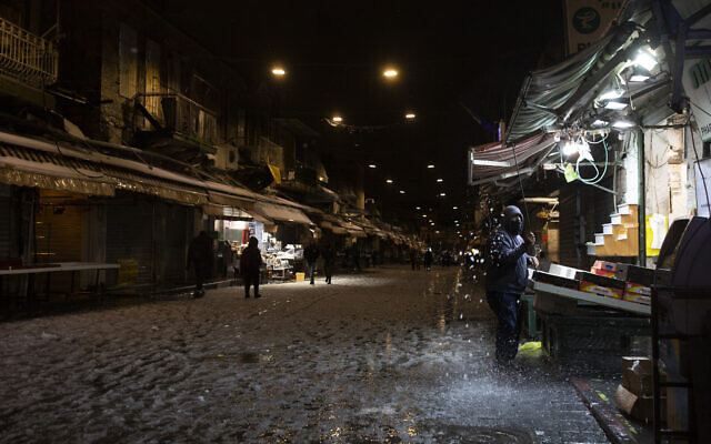 A fruit seller removes snow from his awning at the Mahane Yehuda Market, where many shops closed early due to winter weather in Jerusalem, Febrary 17, 2021. (AP Photo/Maya Alleruzzo) A fruit seller removes snow from his awning at the Mahane Yehuda Market, where many shops closed early due to winter weather in Jerusalem, Febrary 17, 2021. (AP Photo/Maya Alleruzzo)