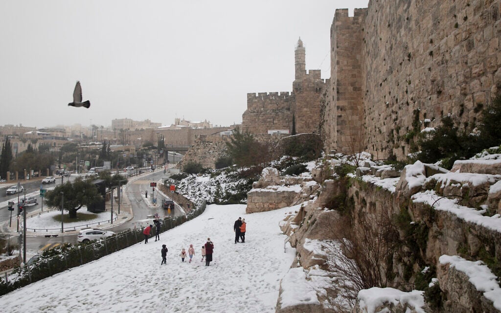 People walk in the the snow next to Jerusalem's Old City walls, Thursday, Feb. 18, 2021. (AP Photo/Oded Balilty)