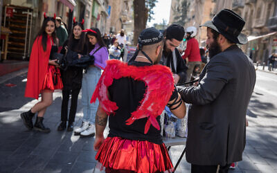 An Israeli dressed up in costume ahead of the holiday of Purim, puts on tefillin in downtown Jerusalem, March 8, 2020 (Olivier Fitoussi/Flash90)