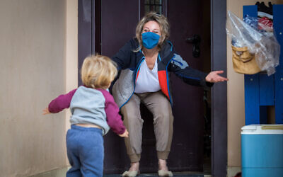 Illustrative: A grandson visits his grandmother at her home in Moshav Haniel in central Israel. She is wearing a face mask as a COVID-19 precaution. (Chen Leopold/Flash90)