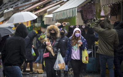 People wearing face masks take cover from the rain as they shop for groceries at the Mahane Yehuda Market in Jerusalem, on February 19, 2021. (Olivier Fitoussi/Flash90)
