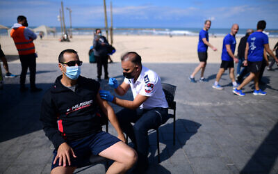Israelis receives a Covid-19 vaccine injection at a Covid-19 mobile vaccine station on the beach in Tel Aviv, February 20, 2021 (Tomer Neuberg/Flash90)
