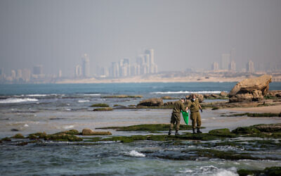 Soldiers clean tar off the Palmachim beach following an offshore oil spill which drenched most of the Israeli coastline, February 22, 2021. (Yonatan Sindel/Flash90)` Soldiers clean tar off the Palmachim beach following an offshore oil spill which drenched most of the Israeli coastline, February 22, 2021. (Yonatan Sindel/Flash90)`
