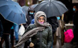 People wearing face masks take cover from rain at the Mahane Yehuda market in Jerusalem, on February 19, 2021. (Olivier Fitoussi/Flash90)