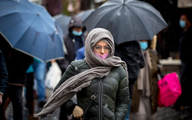 People wearing face masks take cover from rain at the Mahane Yehuda market in Jerusalem, on February 19, 2021. (Olivier Fitoussi/Flash90) People wearing face masks take cover from rain at the Mahane Yehuda market in Jerusalem, on February 19, 2021. (Olivier Fitoussi/Flash90)
