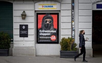 A woman wearing a protective facemask, as a preventive measure against the Covid-19 (the novel coronavirus), walks past a campaign poster, in favour of the 'burqa ban' initiative reading in German: 'Stop extremism!' on March 3, 2021 in the streets of Zurich, ahead of a nationwide vote on March 7, 2021 by Swiss citizen on whether to ban full facial coverings in public places. (Fabrice COFFRINI / AFP)