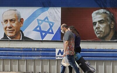 People walk past an electoral billboard for the Likud party bearing a portrait of its leader Prime Minister Benjamin Netanyahu (L), and opposition Yesh Atid party leader Yair Lapid, in Tel Aviv, on March 12, 2021, ahead of the March 23 general election. (JACK GUEZ / AFP) People walk past an electoral billboard for the Likud party bearing a portrait of its leader Prime Minister Benjamin Netanyahu (L), and opposition Yesh Atid party leader Yair Lapid, in Tel Aviv, on March 12, 2021, ahead of the March 23 general election. (JACK GUEZ / AFP)