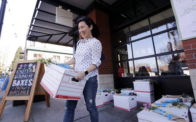 Jessica Choe picks up a 'seder to go' kit packed and left with dozens of others outside a local cafe ahead of her family's Passover meal April 8, 2020, in Seattle. (AP Photo/Elaine Thompson)