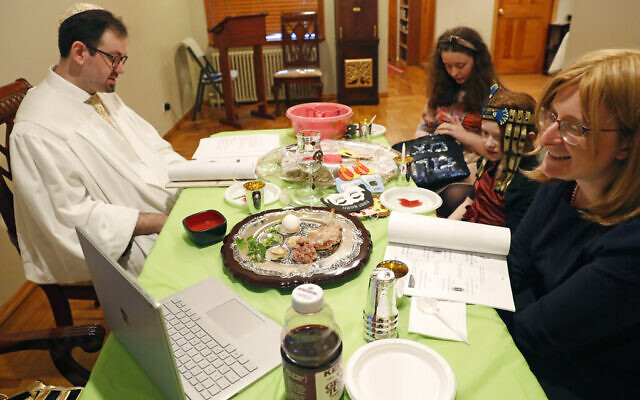 Rabbi Shlomo Segal, left, reads from the Passover Haggadah, a guide to the holiday service, as his wife Adina, right, and daughters Shira, 12, third from right, and Rayna, 8, second right, listen, Wednesday, April 8, 2020, in New York, during the current coronavirus outbreak. The COVID-19 crisis has forced people to stay at home and avoid gathering with others as governmentally-imposed social distancing rules are in place. (AP Photo/Kathy Willens)