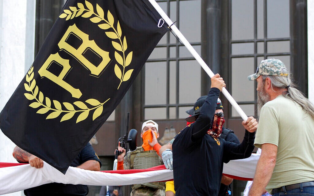 A protester carries a Proud Boys banner while other members start to unfurl a large US flag in front of the Oregon State Capitol in Salem, Oregon, September 7, 2020 (AP/Andrew Selsky). A protester carries a Proud Boys banner while other members start to unfurl a large US flag in front of the Oregon State Capitol in Salem, Oregon, September 7, 2020 (AP/Andrew Selsky).
