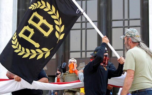 A protester carries a Proud Boys banner while other members start to unfurl a large US flag in front of the Oregon State Capitol in Salem, Oregon, September 7, 2020 (AP/Andrew Selsky). A protester carries a Proud Boys banner while other members start to unfurl a large US flag in front of the Oregon State Capitol in Salem, Oregon, September 7, 2020 (AP/Andrew Selsky).