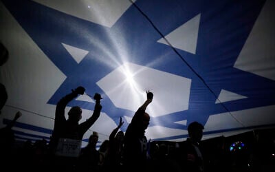 A large Israeli flag is carried during a demonstration against Prime Minister Benjamin Netanyahu In Jerusalem, Saturday, March. 20, 2021.(AP Photo/Sebastian Scheiner)