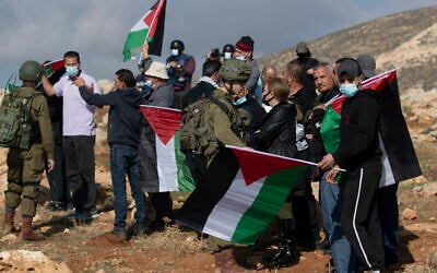 Israeli soldiers stop Palestinian protesters from reaching a Jewish settler outpost, at the outskirts of the West Bank village of Mughayer, north of Ramallah on December 18, 2020. (AP/Nasser Nasser)