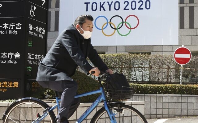 A man wearing a face mask cycles past the logo of the Tokyo Olympics, in Tokyo, Wednesday, Feb. 17, 2021 (AP Photo/Koji Sasahara) A man wearing a face mask cycles past the logo of the Tokyo Olympics, in Tokyo, Wednesday, Feb. 17, 2021 (AP Photo/Koji Sasahara)