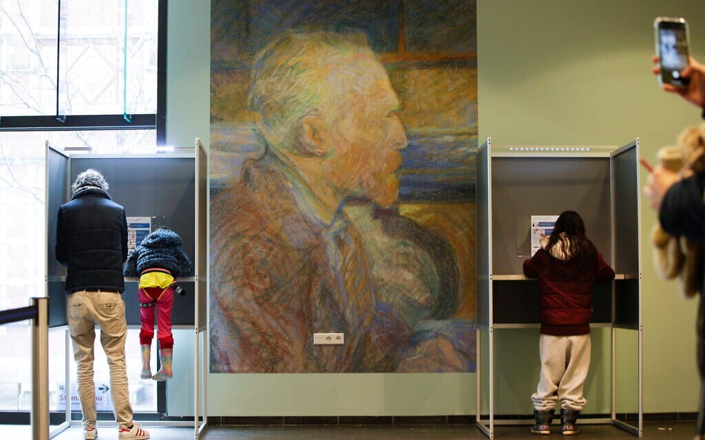 A mother uses her mobile phone to take an image of her husband and child in a voting booth, left, prior to casting their ballot for a general election at the Van Gogh Museum in Amsterdam, Netherlands, Wednesday, March 17, 2021. (AP Photo/Peter Dejong)