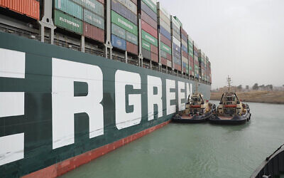This photo released by the Suez Canal Authority on March 25, 2021, shows two tugboats next to the Ever Given, a Panama-flagged cargo ship, after it become wedged across the Suez Canal and blocking traffic in the vital waterway from another vessel (Suez Canal Authority via AP)