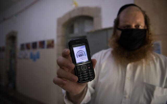 A teacher holding up his cellular phone certificating that it is a 'kosher' one, at the entrance to at an Ultra-Orthodox school in Jerusalem, on May 6, 2020. (Nati Shohat/Flash90) A teacher holding up his cellular phone certificating that it is a 'kosher' one, at the entrance to at an Ultra-Orthodox school in Jerusalem, on May 6, 2020. (Nati Shohat/Flash90)
